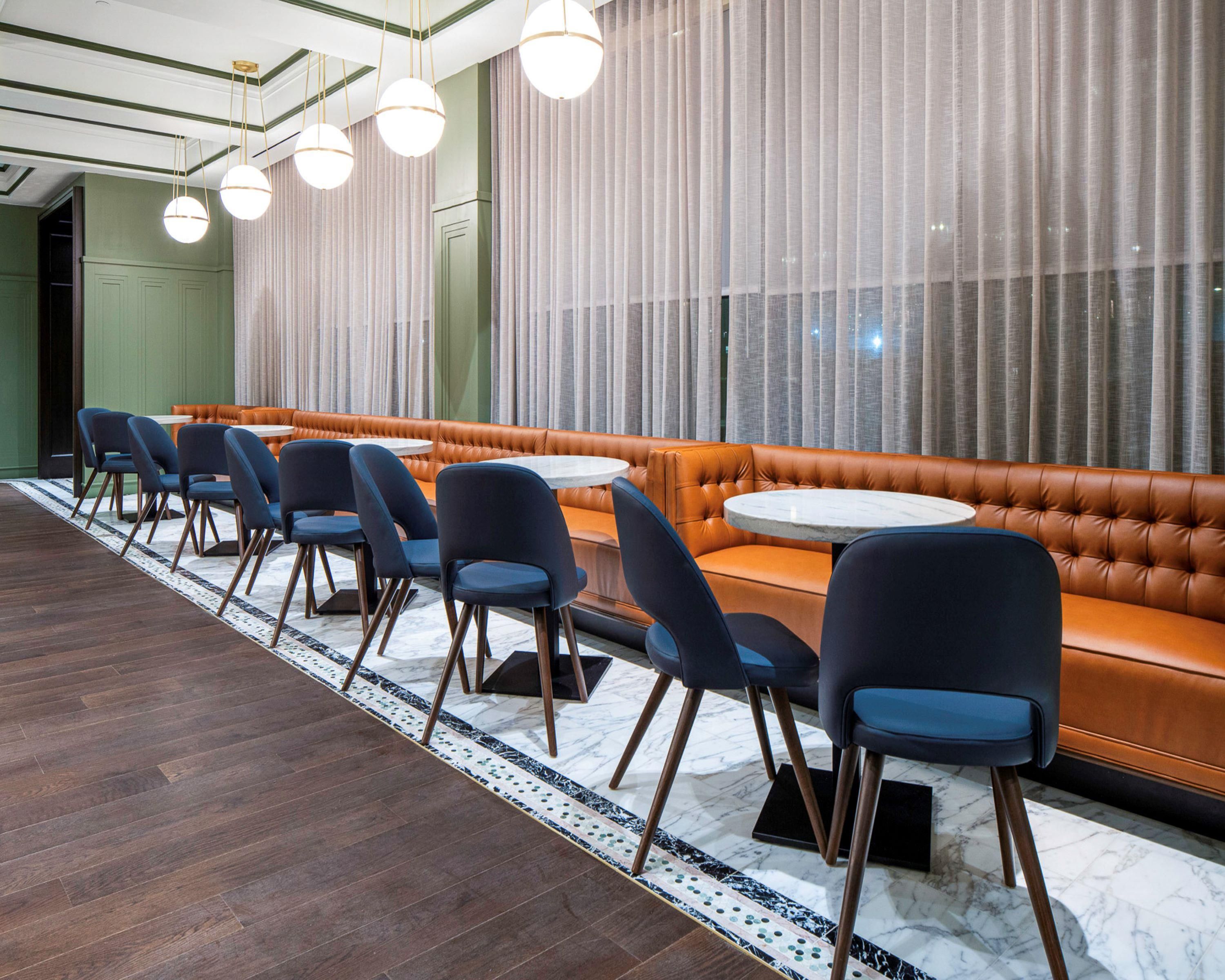 A modern restaurant with a long dining table, blue chairs, and a leather booth.