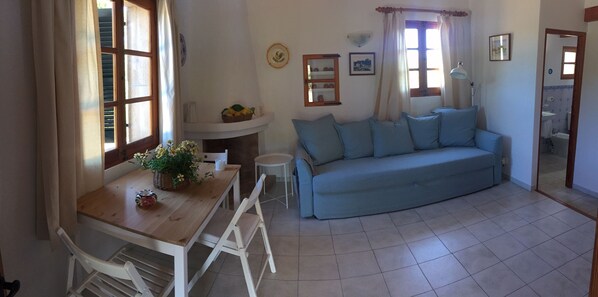 Un salon avec une table à manger en bois, des chaises blanches, un canapé bleu et une petite table d’appoint blanche.