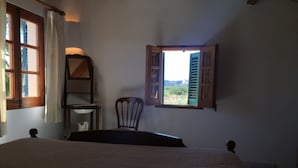 A bedroom with a bed, a chair, a small table, and a window with open shutters. - Lovely villa in Pollença, countryside (pollença)