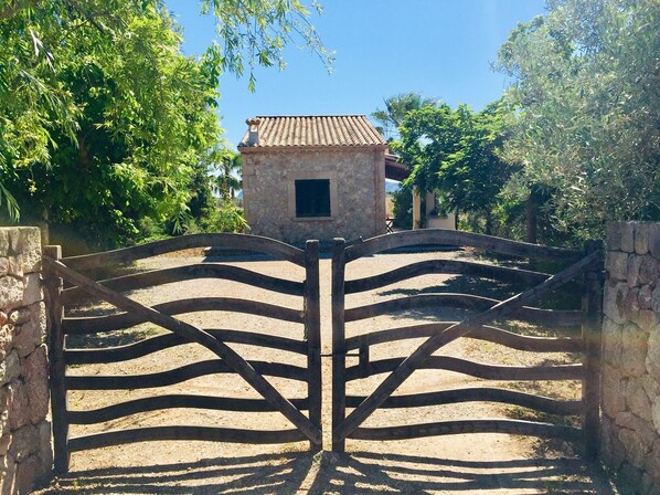 A gated entrance with a stone wall and a tiled-roof building in the background. - Lovely villa in Pollença, countryside (pollença)