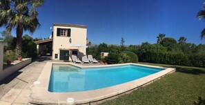 Une piscine avec une terrasse carrelée, un petit bâtiment doté d’une fenêtre et d’un volet, et quelques chaises longues.