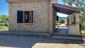 A stone building with a small porch, a window with shutters, and a view of greenery and mountains in the background. - Lovely villa in Pollença, countryside (pollença)