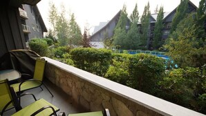 Un balcon avec des chaises vertes, un mur en pierre et une vue sur un immeuble et des arbres.