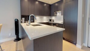 Une cuisine moderne avec des meubles de couleur sombre, un plan de travail blanc et une cuisinière intégrée.