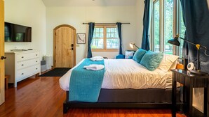 A bedroom with a bed, a desk, a television, a ceiling fan, and a window with curtains.