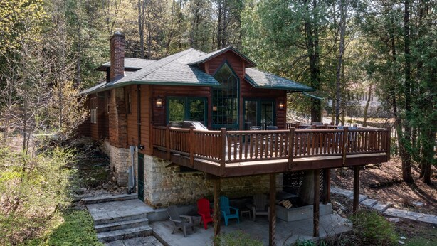 A log cabin with a deck, outdoor seating, and a stone foundation.