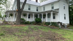 A large, two-story white house with a wrap-around porch, multiple windows, and a chimney. - Private room and bathroom in the heart of Cullman. (Cullman)