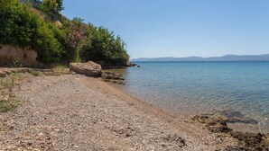 Una playa de arena fina con agua cristalina, un acantilado rocoso y una cadena montañosa en la distancia.