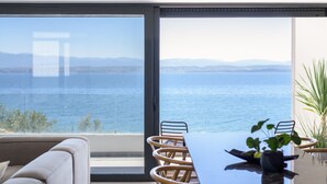 Una habitación moderna con un amplio ventanal con vistas a un cuerpo de agua, una mesa de comedor con sillas y un sofá.