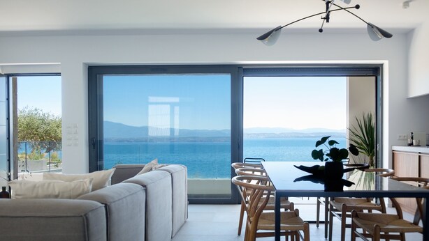 Una sala de estar moderna con una amplia mesa de comedor y sillas, un sofá, y vistas al mar.