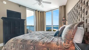 Un dormitorio con una cama grande, un ventilador de techo, un televisor sobre un mueble y vistas al océano.