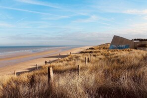 Een strand met een modern gebouw, herkenbaar aan grote ramen en een schuin dak.