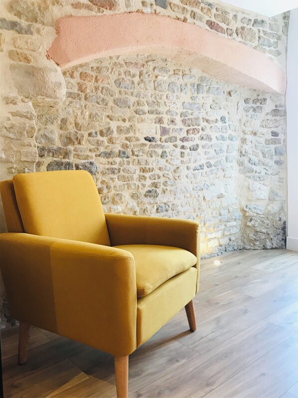 Een mosterdgele fauteuil in een kamer met een stenen muur en houten vloer.