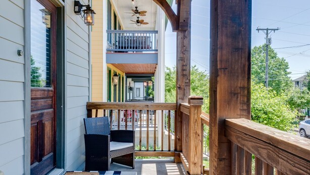 Une véranda avec une balustrade en bois, un ventilateur de plafond, des guirlandes lumineuses et un paillasson.