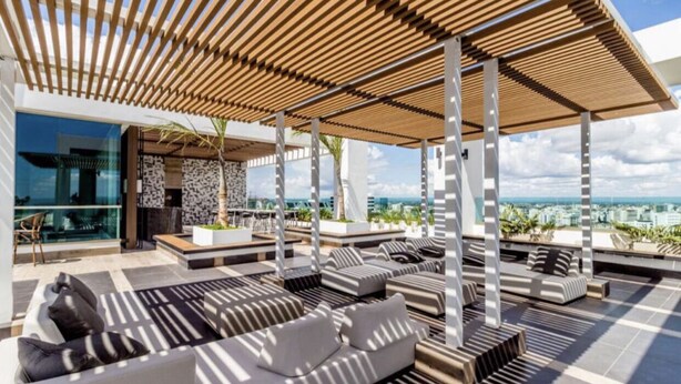 Un salón en la azotea con mobiliario exterior moderno, una pérgola de madera y vistas panorámicas de la ciudad.