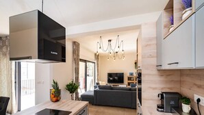 A modern kitchen with a built-in stove, grey cabinetry, and a dining area with a sofa and TV.