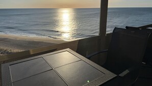 Vista da praia a partir de uma varanda com mesa e cadeiras.