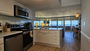 Uma cozinha com uma ilha grande, eletrodomésticos de aço inoxidável e vista para o oceano através de amplas janelas.