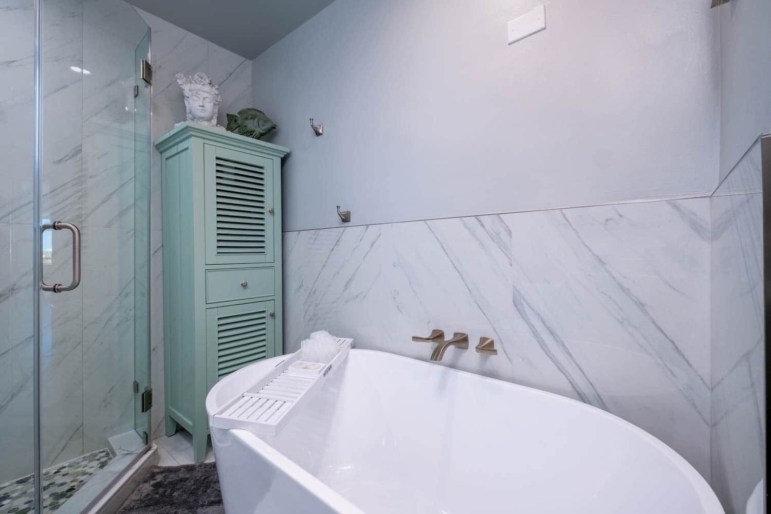 A bathroom with a freestanding bathtub, a glass shower enclosure, and a green cabinet with decorative items.