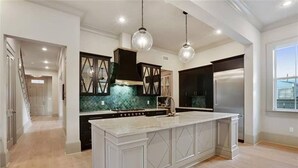 Una cucina moderna con un'isola grande, mobili scuri e illuminazione a sospensione.