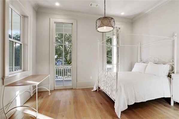 Un dormitorio con una cama con dosel blanco, una mesita de noche pequeña y una ventana con vistas a árboles.