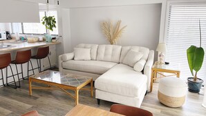 Una sala de estar moderna con un sofá seccional, una mesa de centro de vidrio y una zona de comedor con una mesa y sillas de madera.