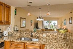 A kitchen with granite countertops, a double sink, wooden cabinets, and pendant lighting. - Scenic 2 Bed Condo by the Beach with Pool - Perfect View (St. Augustine)