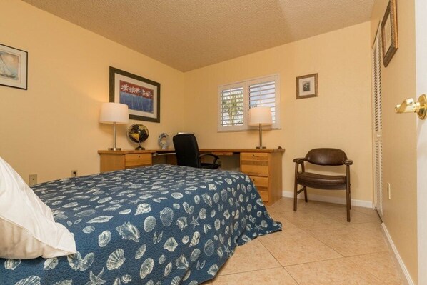 A bedroom with a bed, desk, chair, and a window with blinds.