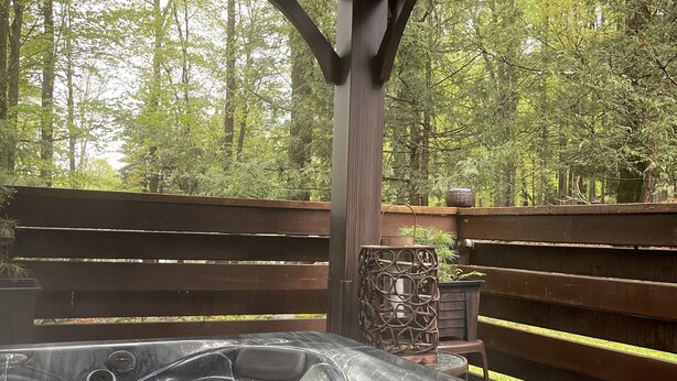 A hot tub in a covered outdoor area with a wooden deck and a forest backdrop. - Perfect getaway from your daily routine!!! (Greentown)