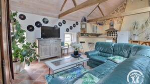 A cozy living room with a sofa, a coffee table, and a TV. There are plants, a kitchen area, and a dining table with chairs. - Keriker - PLOEMEL - Gîte (PLOEMEL)