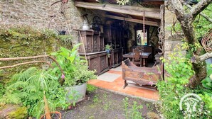 A rustic stone building with a wooden bench and a table, surrounded by lush greenery and potted plants. - Keriker - PLOEMEL - Gîte (PLOEMEL)