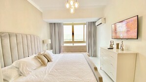 Un dormitorio con una cama grande, un aparador, un televisor y una ventana con cortinas.
