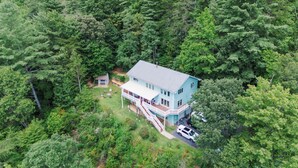 Une maison à deux étages entourée d’une forêt dense.