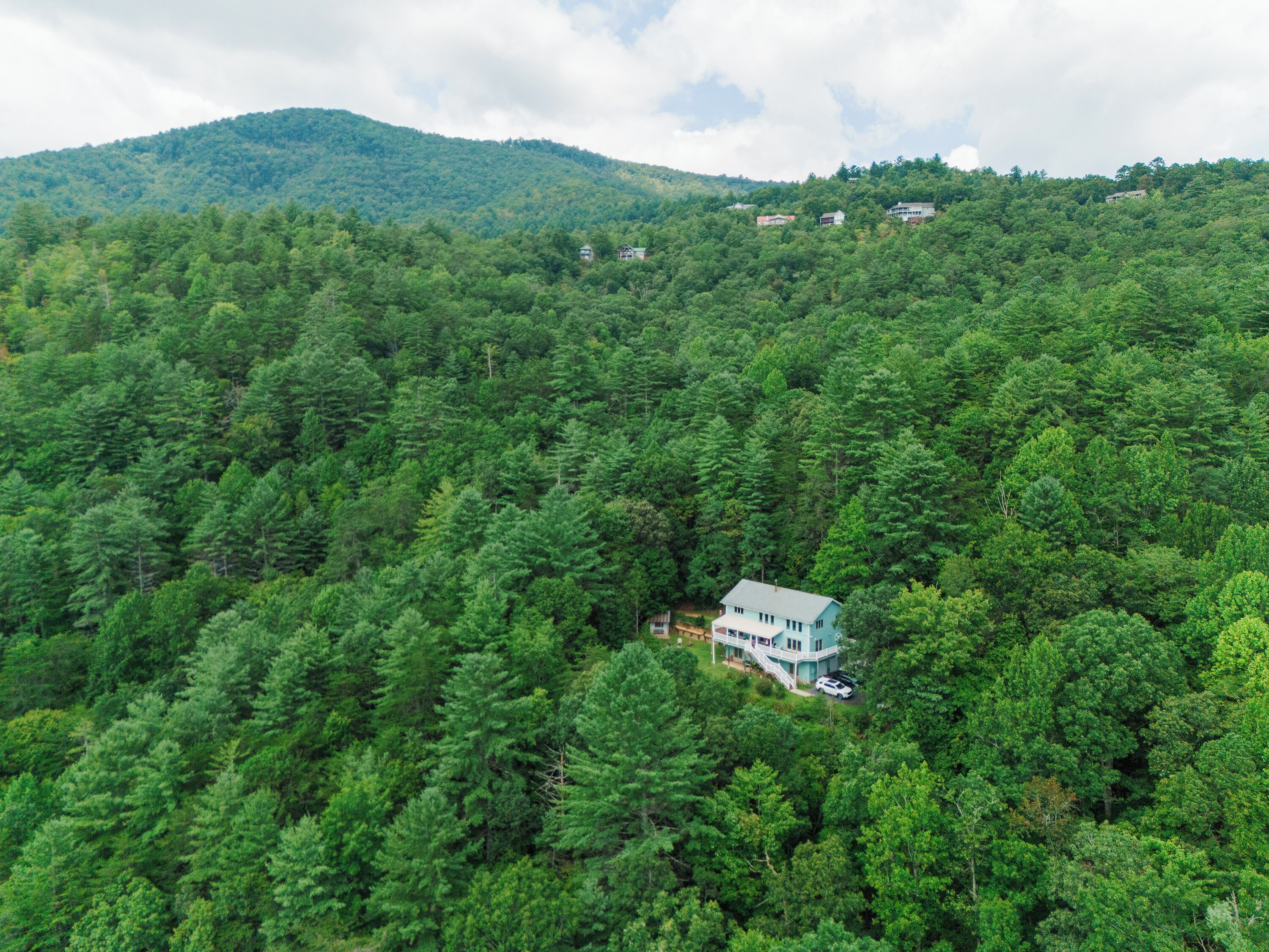 Une maison entourée d’une forêt dense, avec une montagne en arrière-plan.
