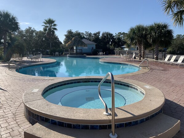 A swimming pool with a hot tub, surrounded by palm trees and lounge chairs.