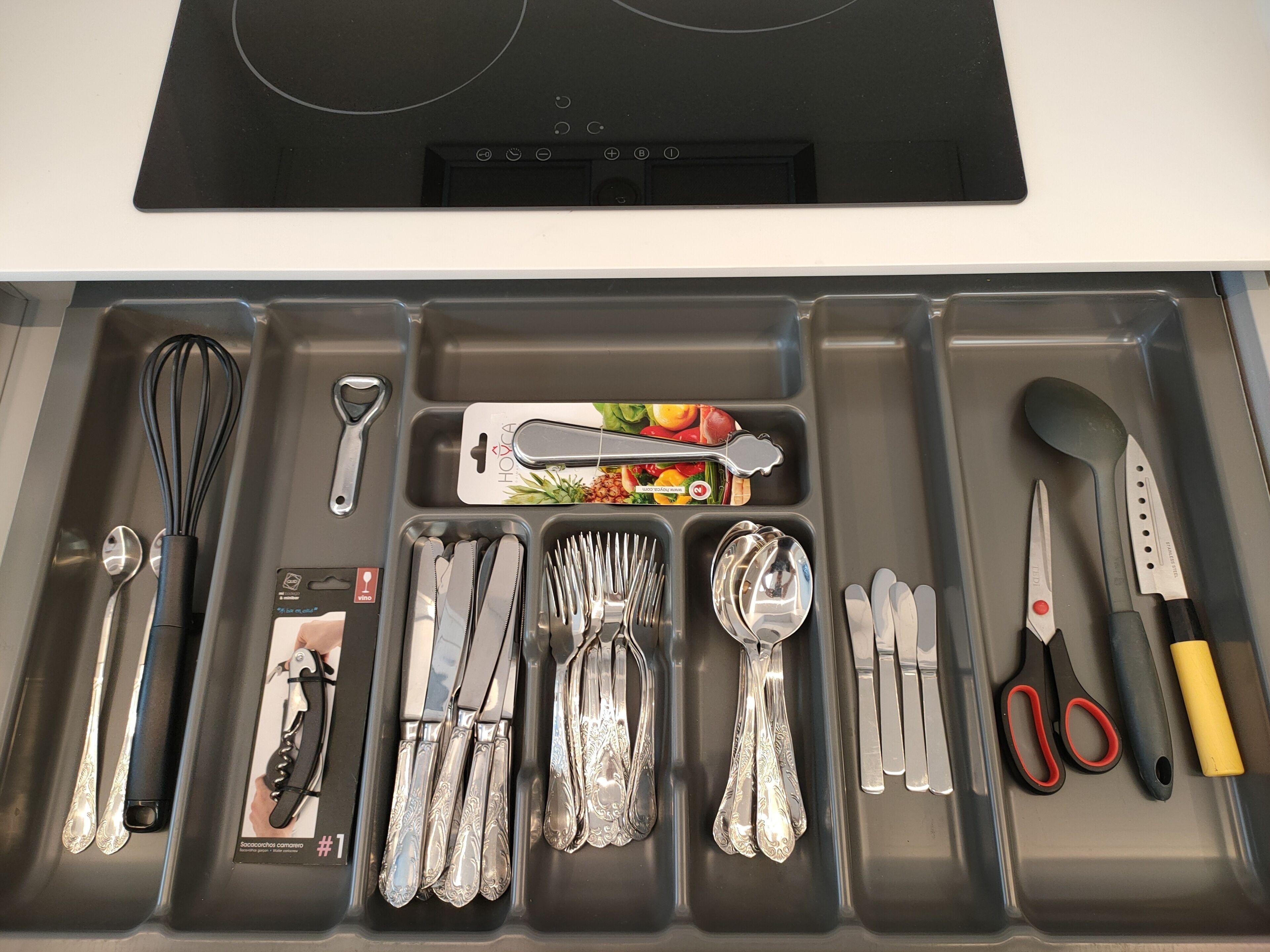 Un cajón con utensilios de cocina, incluyendo batidores, un rallador, cuchillos, cucharas y un par de tijeras.