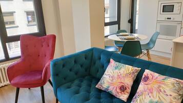 A modern living room with a teal sofa, a red armchair, and a dining area with a table and chairs.