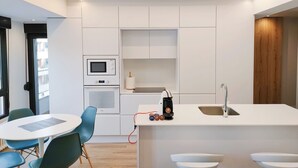 Une cuisine moderne avec des meubles blancs, un four à micro-ondes encastré, une machine à café et une table de salle à manger ronde avec des chaises.