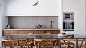 Une cuisine moderne avec une table en marbre noir, des chaises en bois et des appareils électroménagers intégrés.