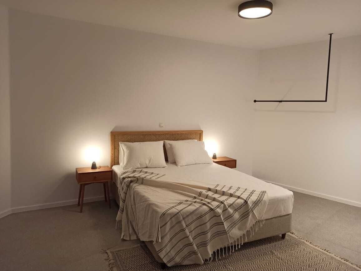 Une chambre à coucher comprenant un lit, deux tables de chevet, une commode, un tapis et un luminaire fixé au mur.
