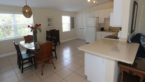 A spacious kitchen with white cabinets, a dining area with a glass table and chairs, and a hanging light fixture. - Silver Sands, Oceanfront - Gulf Beach Resort (Longboat Key)
