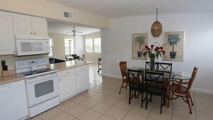 A spacious kitchen with white cabinetry, a microwave, and a stove. There is a dining area with a glass table and chairs, and two potted plants on the wall. - Silver Sands, Oceanfront - Gulf Beach Resort (Longboat Key)