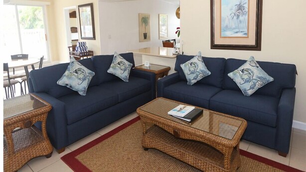 A living room with two blue sofas, wicker coffee tables, and a ceiling fan. - Silver Sands, Oceanfront - Gulf Beach Resort (Longboat Key)