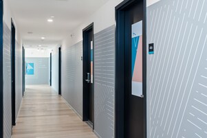 Un corridoio moderno di un albergo con pavimento in legno, porte di colore scuro e una parete decorata con un motivo geometrico.