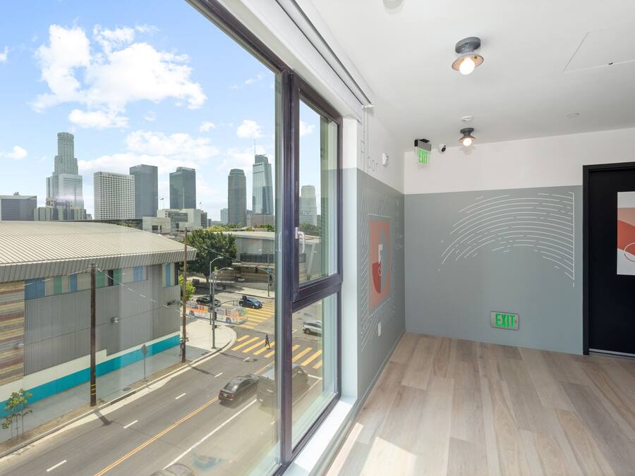 Interior moderno de hotel con amplios ventanales que ofrecen vista panorámica de la ciudad, suelo limpio y señal de salida en la pared.