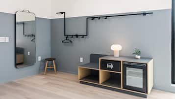 A modern room with a wooden floor, a built-in cabinet with a microwave, a small stool, a wall-mounted mirror, and a hanging coat rack.
