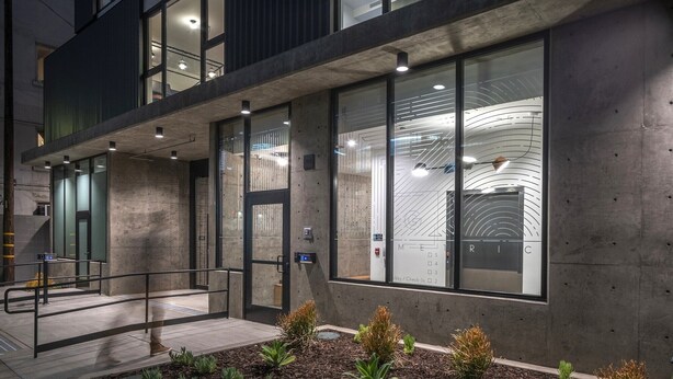 A modern building with large windows, a concrete facade, and a small garden area with various plants. - The Metric (Los Angeles)
