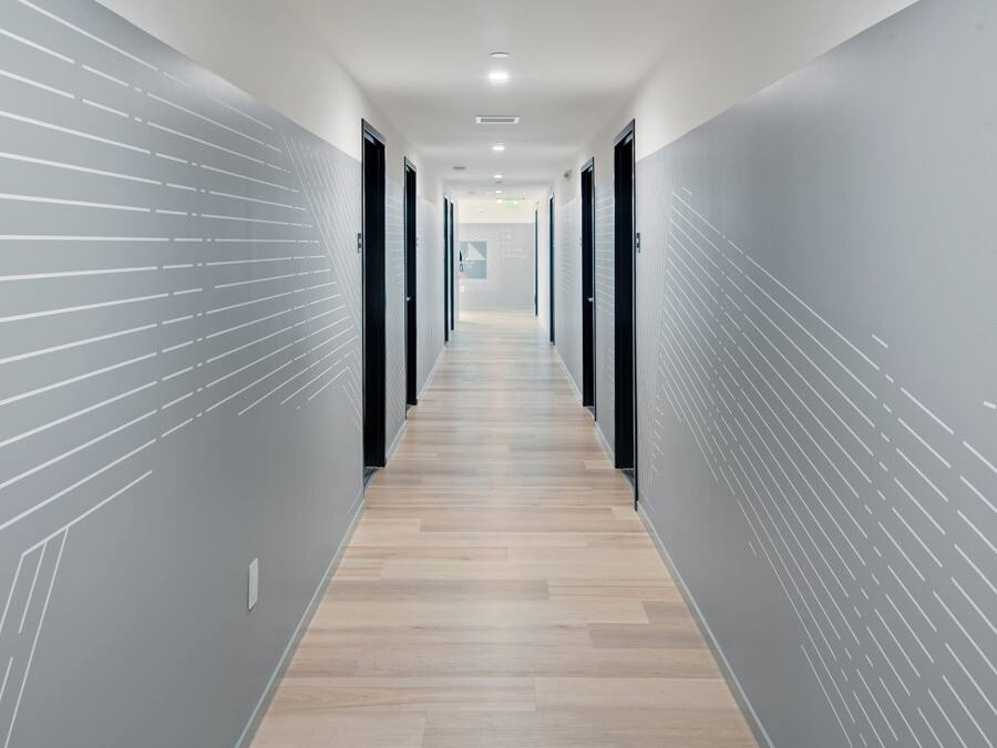 Un couloir moderne avec un plancher en bois et des murs gris ornés d’un motif discret.