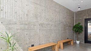 A reception area with a concrete wall, a 'welcome' sign, two wooden benches, a potted plant, and a door. - The Metric (Los Angeles)