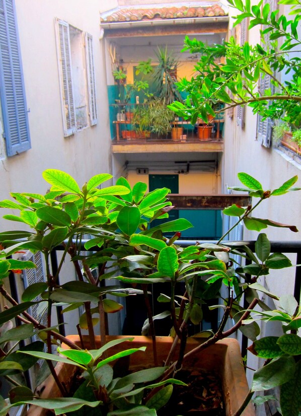 A balcony with potted plants, a railing, and a view of a building with a tiled roof and shutters.